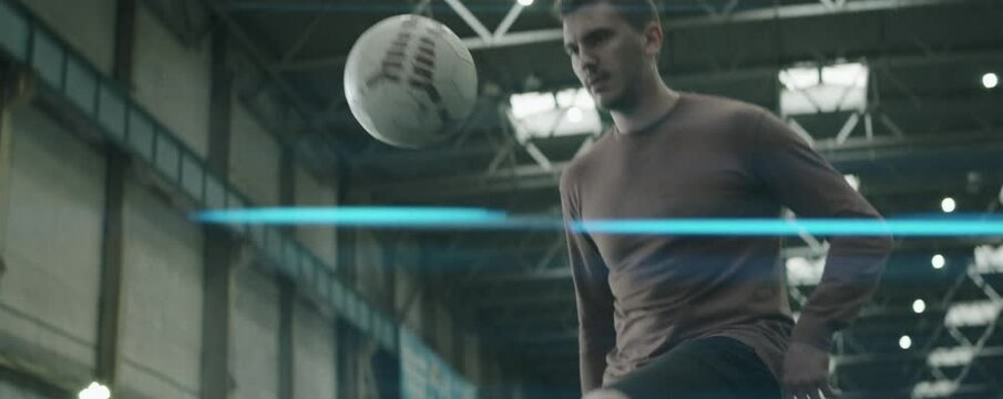 Anamorphic shot of skillful soccer player juggling ball while training on indoor football field