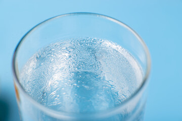 Glass of pure cold water on a blue background close-up wet.