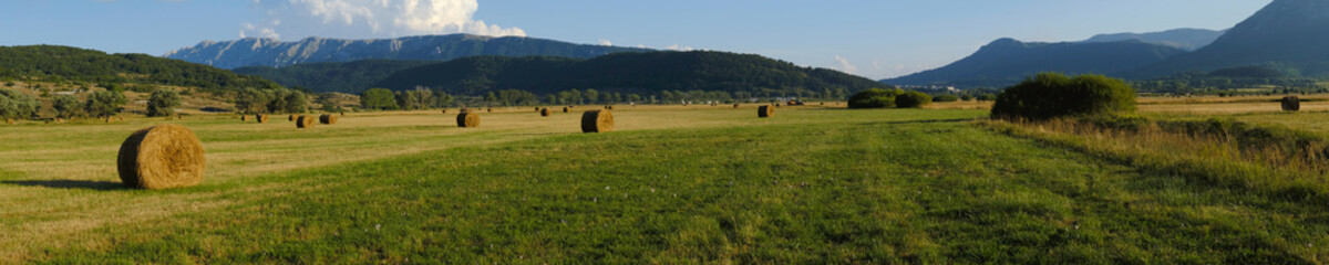 Many hay bales over the rural fields at Rocca di Mezzo upland , with high mountains on the background , Abruzzo , Italy