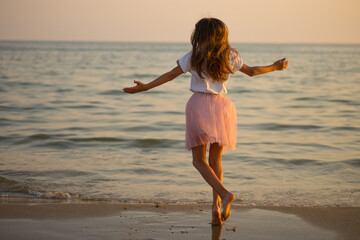 Happy little girl is spinning and dancing on the beach on a Sunny day.