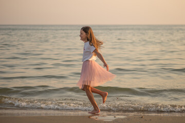 Happy little girl is spinning and dancing on the beach on a Sunny day.