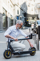 Fototapeta na wymiar mature man adjusting electric scooter on street