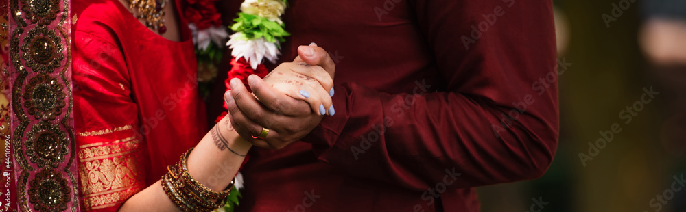 Wall mural cropped view of indian man holding hands with bride with mehndi in sari, banner