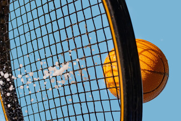 A hit with a tennis racket to a wet ball, on a background of blue sky, close up view