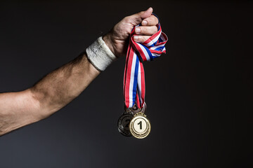 Plakat Arm of elderly athlete holding three gold, silver and bronze medals on a dark background. Sports and victory concept.