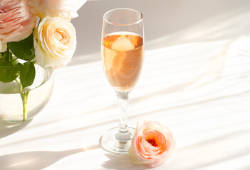 A glass of semi-sweet pink wine Pinot rose . Next to a bouquet of antique terry roses Pierre de Ronsard, Eden roses. Striped shadows on a white background. High quality photo
