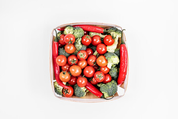 wooden basket full of cherry tomatoes broccoli pieces and red hot chili peppers on white background