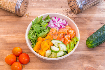 Poke bowl with pumpkin, marinated salmon, avocado, chopped red onion, arugula and chopped cucumber on wooden table