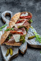 Ciabatta sandwich with prosciutto, sun-dried tomatoes, gherkins, parmesan and arugula. vertical image. top view