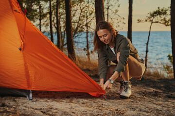 Lively woman installing an orange tent in the woods