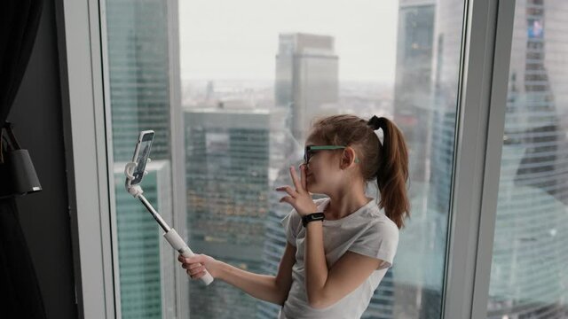 Modern teenage girl taking a selfie near the window in a modern apartment overlooking the city from a high floor. Technology concept, new generation of youth