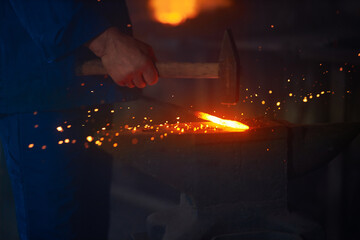 Fototapeta premium Experienced blacksmith manually forging molten metal with hammer on anvil. Close up of string male hands. Forge workshop. 