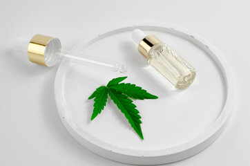 A bottle of hemp oil, a hemp leaf and a dropper on a white saucer. Natural hemp cosmetics. Cosmetics CBD oil