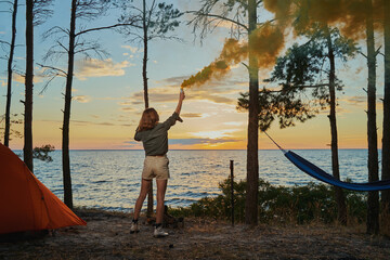 Woman in forest is waving smoke flare