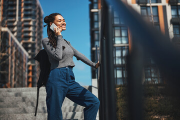 Joyful female talking on the smartphone on a concrete staircase