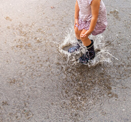 Child in rubber boots hops puddle in summer. Summer rain. Kind in Gummistiefeln hüpft Pfütze im Sommer. Sommerregen.