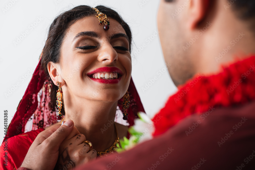 Wall mural happy indian bride in headscarf holding hands with blurred bridegroom isolated on white - Wall murals