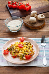 Risotto with mushrooms and cheese in a plate on a napkin on a wooden background near rice and vegetables.