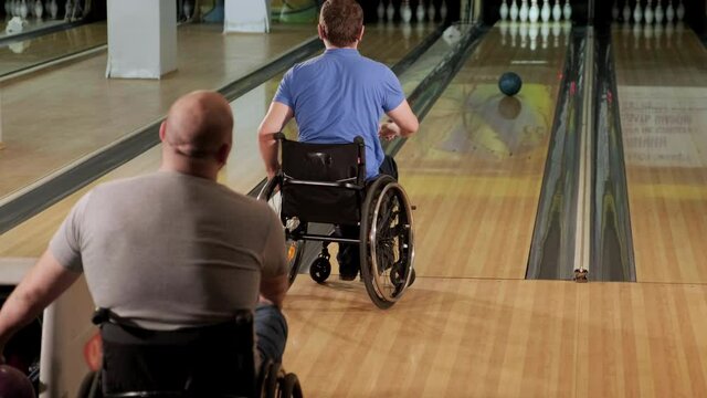 Two young disabled men in wheelchairs playing bowling in the club