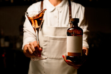 glass with splashing alcoholic cocktail and bottle in the hands of woman.