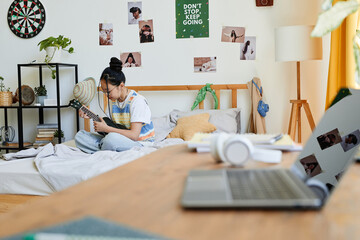 Portrait of Asian teenage girl playing ukulele while sitting on bed in cozy room, copy space