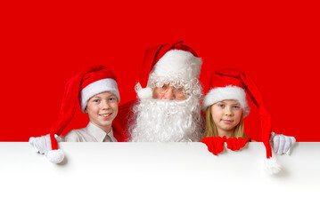 satna claus with funny children in red christmas gnome hats peeking out from behind a blank white banner, mockup and copy space