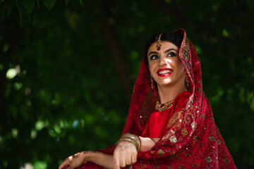 pleased indian bride in red sari and traditional headscarf with ornament