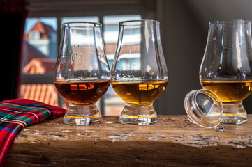 Dram of single malt scotch whisky served in tasting glass with view on old window and houses and red tartan