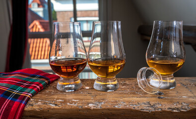 Dram of single malt scotch whisky served in tasting glass with view on old window and houses and red tartan