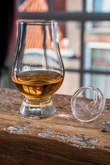 Dram of single malt scotch whisky served in tasting glass with view on old window and houses