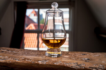 Dram of single malt scotch whisky served in tasting glass with view on old window and houses
