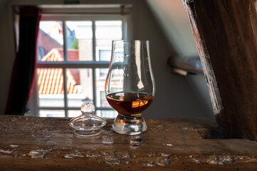 Dram of single malt scotch whisky served in tasting glass with view on old window and houses