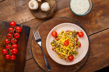 Risotto with mushrooms and cheese on a wooden background near rice and vegetables.