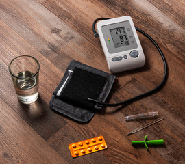 tensiometro, pastillas con un vaso de agua y termometro, sobre una mesa de madera