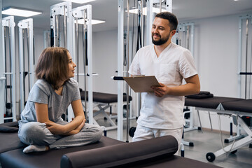Obraz premium Little girl listens to male doctor on massage bed in rehabilitation center. Medical report review