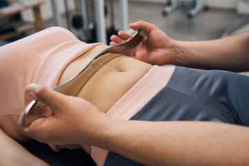 Chiropractor massages woman using IASTM tool for scraping muscles in rehab clinic gym closeup