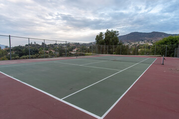 Tropical clouds at sunrise diffuse the morning light onto the doubles lines of the tennis hard court