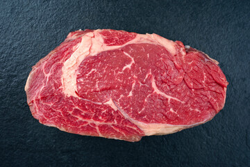 Raw dry aged wagyu rib-eye beef steaks offered as close-up on a black board with copy space
