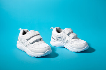 side view of two white unisex sneakers with velcro fasteners for quick shoeing on a blue paper background.