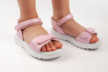 Pink children's sandals made of shiny leather with Velcro fasteners, flat white soles, isolated on a white background. A pair of fashionable children's sandals for a comfortable walk. 