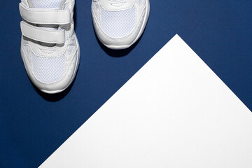  Photo of a pair of white children's sports sneakers made of leather and sewn with fabric with a velcro fastener with shadows on a blue, white background with a place to copy text or design. 