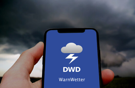 Logo der DWD WarnWetter App wird auf einem Smartphone angezeigt, im Hintergrund ein aufziehendes Gewitter, Unwetter, Unwetterwarnung, Extremwetter