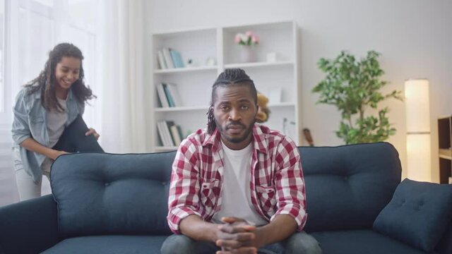 Tired father sitting on sofa while daughters playing with pillows, parenting
