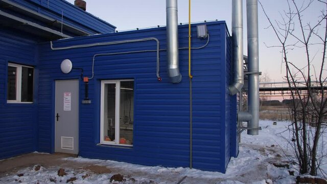 Entrance to blue workshop building with metal chimneys against reservoirs at wastewater treatment station in winter evening