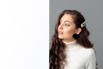 beautiful sensual woman with long curly hair shows a blank banner, isolated on gray, copy space