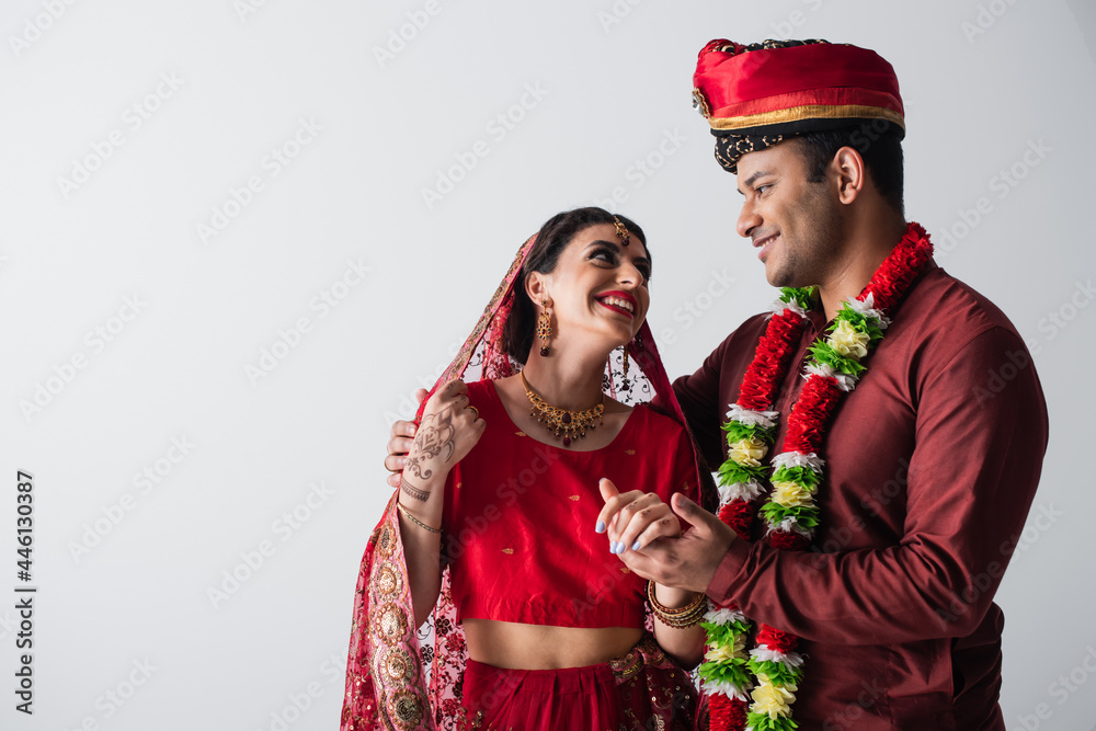 Wall mural joyful indian husband and wife in traditional clothing holding hands isolated on grey