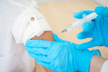 A doctor in blue latex gloves vaccinates a patient against a coronavirus, a close-up shot, a...