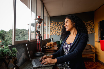 Hermosa latina tele trabajando desde un hostal con una computadora portátil muy sonriente - obrazy, fototapety, plakaty