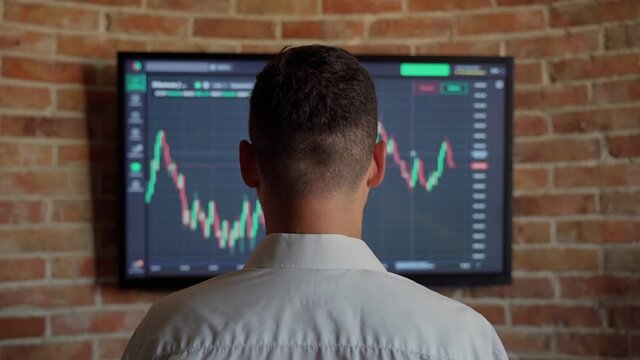 Man trader looking at graph currency bank money indoors. Male businessman person check status online money finance at screen. He dressed white shirt. Quotes eth and btc at stock exchange market chart