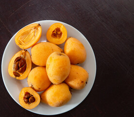 Ripe loquats on white plate on dark rustic background top view. One cut in half showing the inside of the fruit with the seeds ( Eriobotrya japonica )